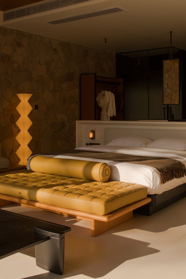 Кровать в сьюте с мягкой желтой банкеткой и каменной стеной ALAN RESORT