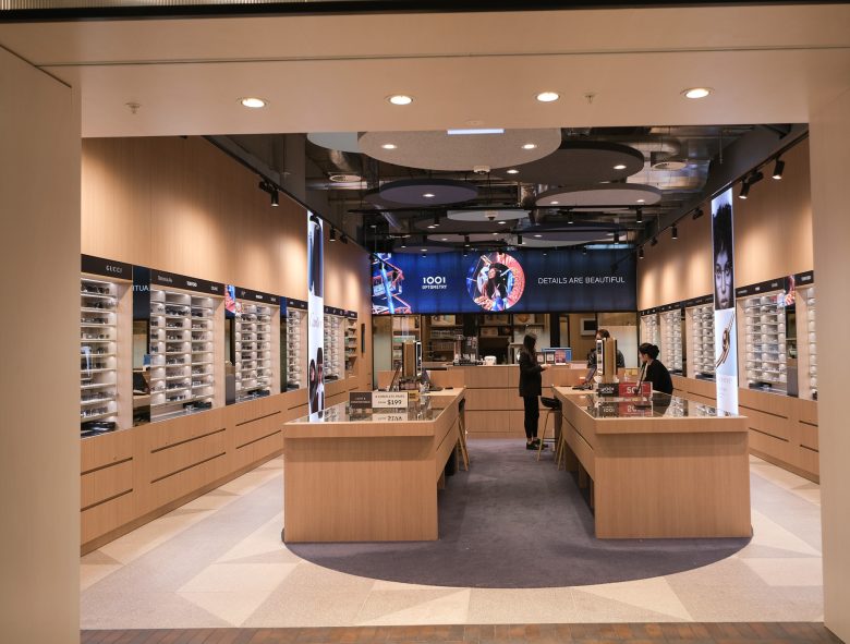 Вид из входа на симметричный зал с витринами и медиаэкраном 1001 Optometry store design