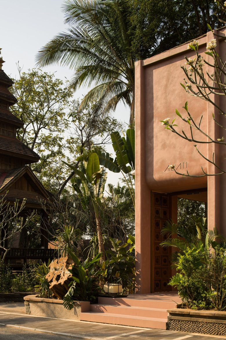 Главный вход ALAN с розовой штукатуркой, деревянной дверью и тропическими растениями ALAN RESORT