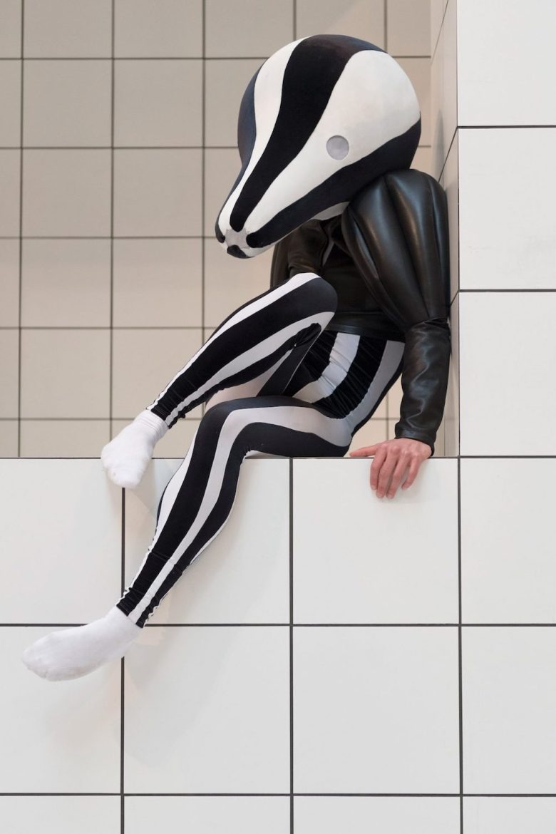 Фигура в полосатом костюме сидит на плиточной конструкции Tate Britain Exhibition